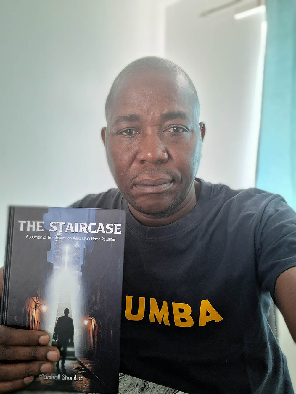 Author Marshall Shumba holding a copy of his latest book 'The Staircase'